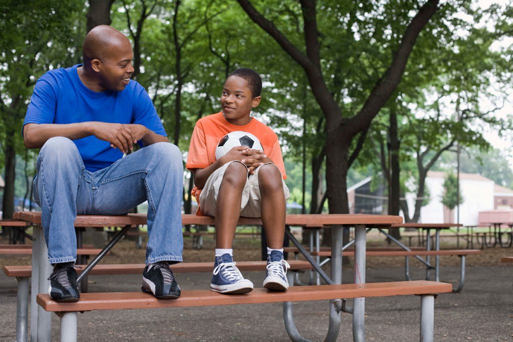 father and son sitting on picnic table while holding a soccer ball