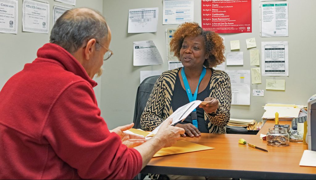 woman helping older man by giving him a form to fill out
